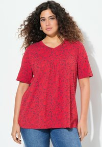 Maglietta rossa con scollo a V e maniche corte, caratterizzata da un motivo astratto nero. Realizzata in materiale leggero e testurizzato.