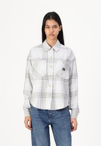 Camisa de botão em padrão xadrez branco e cinza, com dois bolsos frontais e mangas longas, feita de um tecido leve. Possui botões castanhos na pala.