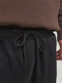 Pantalones de chándal negros con cierre de cordón. Tejido suave con una textura lisa. La cinturilla es acanalada y se ajusta cómodamente a las caderas.