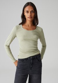 Langärmliges, hellgrünes, eng anliegendes Oberteil mit Rundhalsausschnitt, kombiniert mit dunkelgrauen Jeans. Glatter Stoff und schlankes Design.