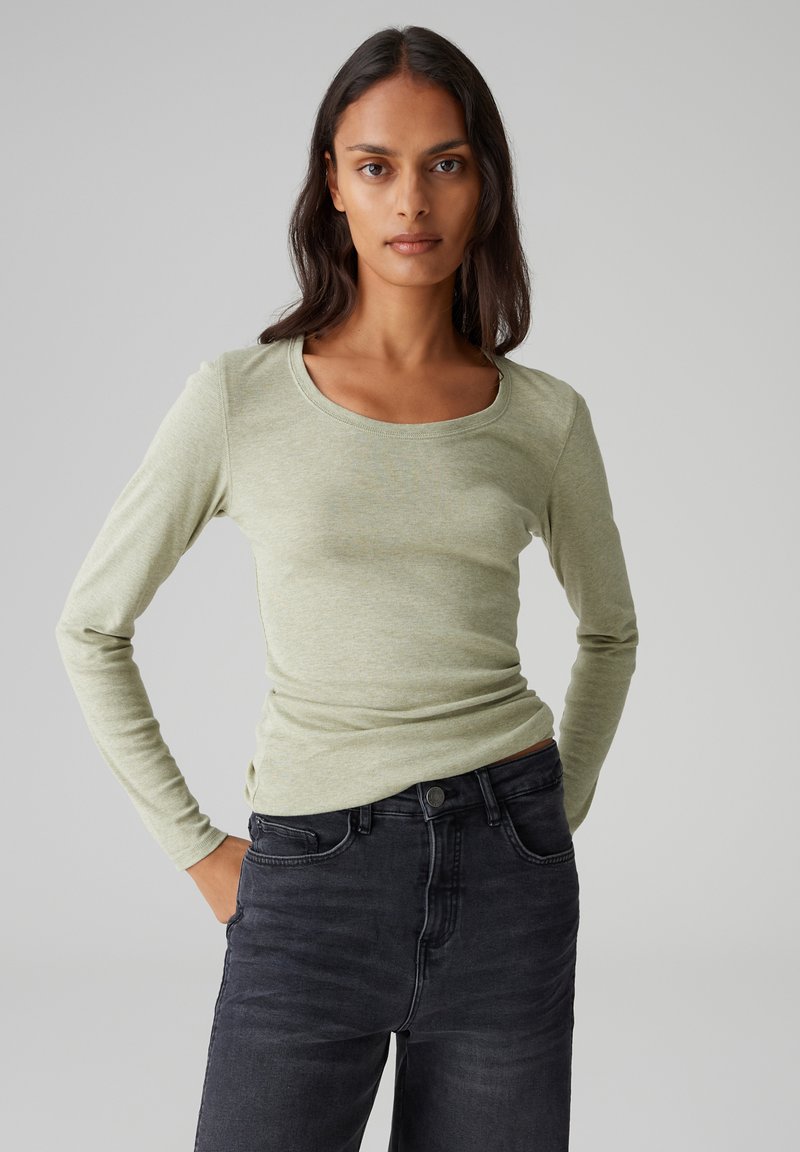 Langärmliges, hellgrünes, eng anliegendes Oberteil mit Rundhalsausschnitt, kombiniert mit dunkelgrauen Jeans. Glatter Stoff und schlankes Design.