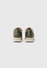 Vue arrière de baskets vert olive avec des accents beiges, présentant une semelle striée blanche et marine à couches et des détails en cuir lisse.