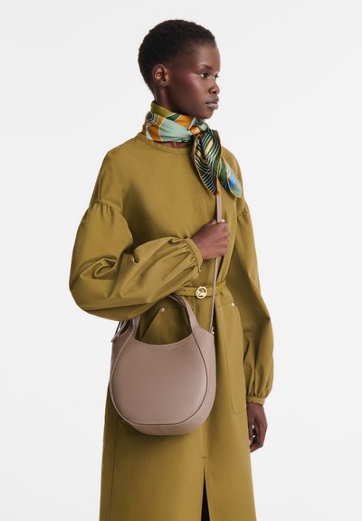 Beige leather handbag with a rounded shape and textured finish, paired with a green and patterned silk scarf and a mustard dress.