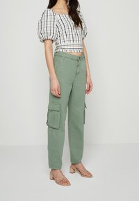 Vit och svart rutad crop top med puffärmar, parat med ljusgröna cargobyxor med sidofickor. Beiga klackar med remmar.