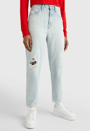 Lichtblauwe distressed jeans met een gescheurde knie, gecombineerd met witte sneakers met een plateauzool en een rood shirt met lange mouwen.