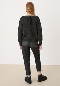 Czarny sweter dzianinowy z szerokim dekoltem z tyłu, związany pod szyją. Połączony z ciemnymi zwężanymi dżinsami i czarnymi teksturowanymi botkami za kostkę.