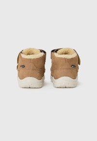 Beżowe zamszowe buty typu high-top z miękkim futerkiem w środku, z rzepami i białą gumową podeszwą; minimalne przeszycia i akcenty z logo.