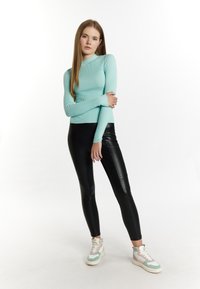 Helles blaues, geripptes Langarmoberteil, kombiniert mit schwarzen, künstlichen Lederleggings und mehrfarbigen High-Top-Sneakern. Einfaches und figurbetontes Design.