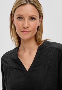 Chemise en lin noir avec un décolleté en V, des détails de patte de boutonnage subtils et une coupe décontractée. Tissu doux au toucher avec une finition lisse.