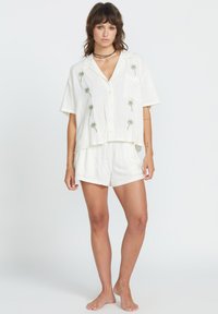 Chemise blanche à manches courtes avec broderie de palmiers verts, associée à un short blanc à cordon de serrage. Tissu doux, coupe décontractée.