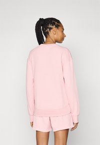 Sweatshirt côtelé rose clair avec une coupe décontractée, doté de manches longues et d'un col rond, associé à un short assorti.
