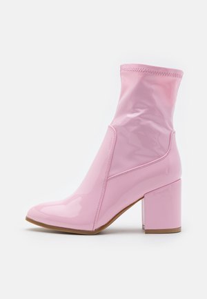 Bottines roses à cheville avec une finition laquée brillante, au design angulaire, talon carré et haut en tissu élastiqué, présentant des détails de couture sans couture.