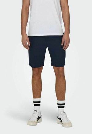 Pantalones cortos azul marino de corte recto, hechos de una tela ligera, combinados con una camiseta blanca, calcetines a rayas y zapatillas casuales.