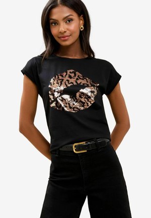 Sort bomulds T-shirt med et design af sølv- og brunt leopardprint læbe i palietter, med rullede ærmer og afslappet pasform. Sorte jeans og bælte synlige.