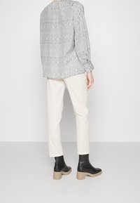 Camicia a maniche lunghe grigia a fantasia abbinata a pantaloni bianchi a gamba dritta e stivaletti neri con tacco alla caviglia con suola beige.