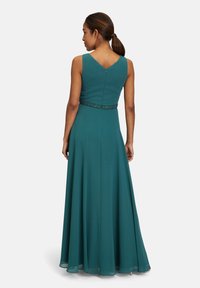 Türkiz esti ruha, amely illeszkedő felsőrésszel, ujjatlan kialakítással és gyöngyökkel díszített derékkal rendelkezik. A szoknya sima textúrával a földig ér.