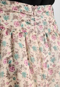 Falda floral con un fondo beige, adornada con flores rosas y teal. Fabricada en una tela ligera, cuenta con pliegues y un cierre de cremallera en la parte posterior.