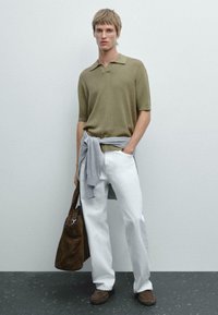 Polo shirt a coste verde oliva, pantaloni bianchi, maglione grigio chiaro annodato in vita, borsa in suede marrone e mocassini abbinati.