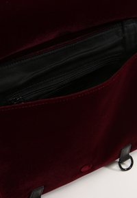 Bolso de terciopelo burdeos con interior negro. Cuenta con un bolsillo con cremallera, textura suave y detalles metálicos.