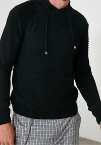 Pull noir en maille avec un col montant et un cordon de serrage ajustable. Présente des rayures horizontales texturées ainsi que des poignets et un ourlet côtelés.