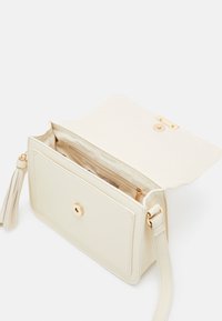 Borsa a tracolla rettangolare color crema con patta aperta che mostra la tasca con zip interna, chiusura magnetica in tono dorato e nappina.