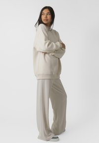 Kreem värvi ülemsuuruses särk ribiteippidega, koos heleda beeži laia jalgadega pükstega. Mõlemad on valmistatud pehmest ja siledast kangast ning neil on mugav lõige.