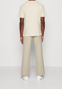 Beige cotton t-shirt paired with light-colored plaid wide-leg trousers. Tennis shoes with white upper and red accents complete the outfit.