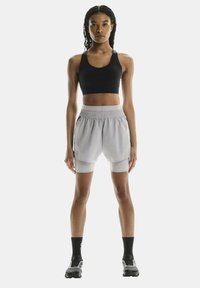 Hellgraue Sportshorts mit integrierten Leggings, elastischem Bund und Seitentaschen, kombiniert mit einem schwarzen, taillierten Tanktop und schwarzen Socken.