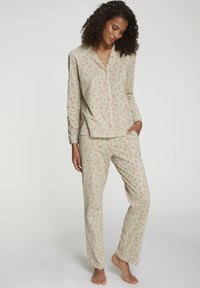 Frau steht barfuß und trägt langärmligen, beigen Schlafanzug mit roten und weißen Zuckerstangenmustern.