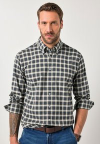 Camicia button-up a quadri nei toni beige, blu navy e verde; presenta un colletto allargato e maniche arrotolate. Realizzata in cotone con una texture liscia.