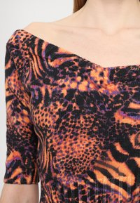 Off-shoulder kjole i svart, oransje og lilla dyreprint med korte ermer og teksturert strikket stoff. Har varierte mønstre.