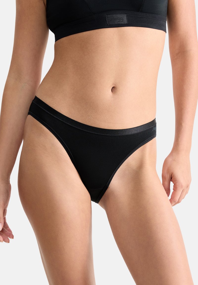 Vrouw in zwarte naadloze bikini-achtige onderbroek en bijpassende zwarte sportbeha, weergegeven van het midden van de romp tot boven de dijen.