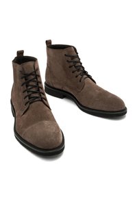 Brązowe zamszowe botki za kostkę z czarnymi sznurówkami, okrągłymi noskami i płaskimi podeszwami. Charakteryzują się gładką teksturą oraz wzmocnioną osłoną palców.