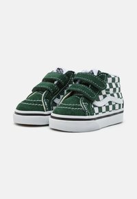 Zapatillas altas de ante verde con un patrón a cuadros blancos, cintas de Velcro y detalles negros sobre una suela de goma blanca.
