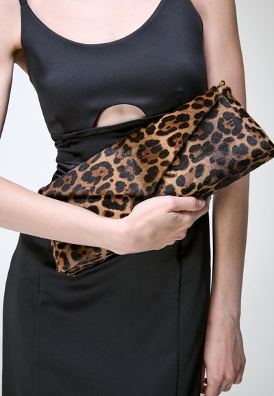 Personne en robe noire tenant une grande pochette à motif léopard, les mains reposant au niveau de la taille.