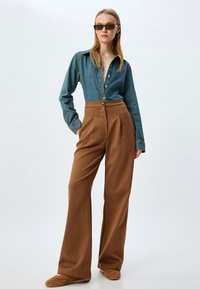 Chemise en denim avec fermeture à boutons et manches longues, associée à un pantalon marron taille haute et à jambes larges. Tissu texturé et coupe décontractée.