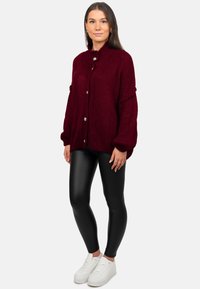 Cardigan en maille bordeaux avec un col montant, de gros boutons et des manches larges, assorti à des leggings noirs et des baskets blanches.