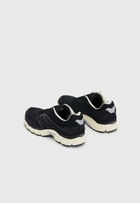 Zapatillas de running negras con parte superior de malla, entresuela blanca y acentos grises. Presenta un talón reforzado y suela texturizada para mayor tracción.