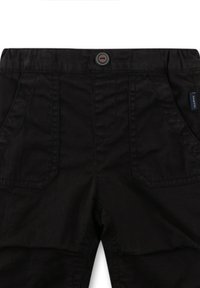 Schwarze Hose mit Knopfverschluss, zwei Vordertaschen und einem kleinen Logosticker an der Seite. Glattes Material mit minimaler Textur.