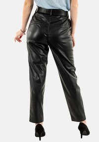 Pantalones de cuero sintético negros con una textura suave, cintura alta y dos bolsillos traseros. Estilizados con un cinturón y combinados con tacones altos negros.