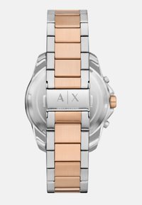 Hõbe- ja roosakuldne metallkellapael, mis sisaldab läikivaid ja harjatud linke, graveeritud logo detaile ja tekstureeritud pinda.