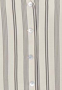 Camicia beige a maniche lunghe con bottini verticali neri, bottoni perlacei e una texture di tessuto liscia con una caduta morbida.