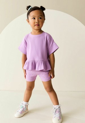 Lavendelfarvet ribbet todelt sæt med peplumtopp og mønstrede shorts, der har et tekstureret stof og farverige sneakers med snørebånd.