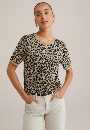 Leopard-print knitted short-sleeve top in beige and black with a round neckline and button details. Paired with light-colored trousers and a black belt.