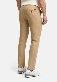 Chinos caqui de corte slim, con una textura suave, bolsillos traseros con botones y combinados con zapatillas deportivas blancas.