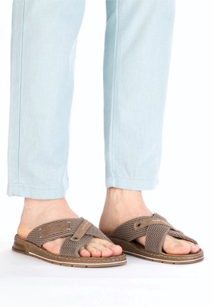 Brown mesh slide sandals with cross-strap design, textured surface, and rubber sole. Paired with light blue cropped pants.