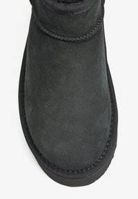 Czarny zamszowy botek za kostkę o gładkiej teksturze, zaokrąglonym kształcie i przeszyciach wzdłuż kołnierza oraz górnej krawędzi. Podeszwa z gumy.