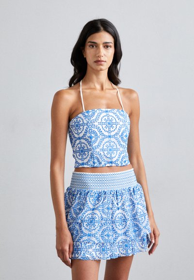 Modrý a bílý vzorovaný crop top s halter řemínky, doplněný o odpovídající rozšířenou sukni s úpletem v pase a volánkovým lemem.