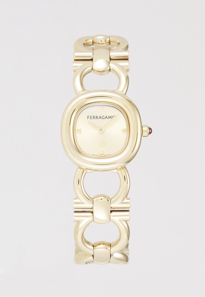 Kuldtooni Ferragamo kell ümmarguse korpuse, lingitud bändi disaini ja heleda taustaga, millel on tunni näitajad ja logo.