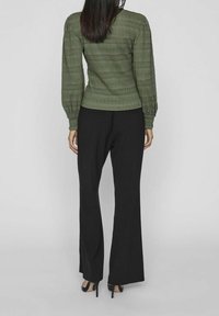 Grünes gemustertes Strickoberteil mit langen Ärmeln, kombiniert mit schwarzen ausgestellten Hosen und schwarzen hohen Absätzen, von hinten betrachtet.